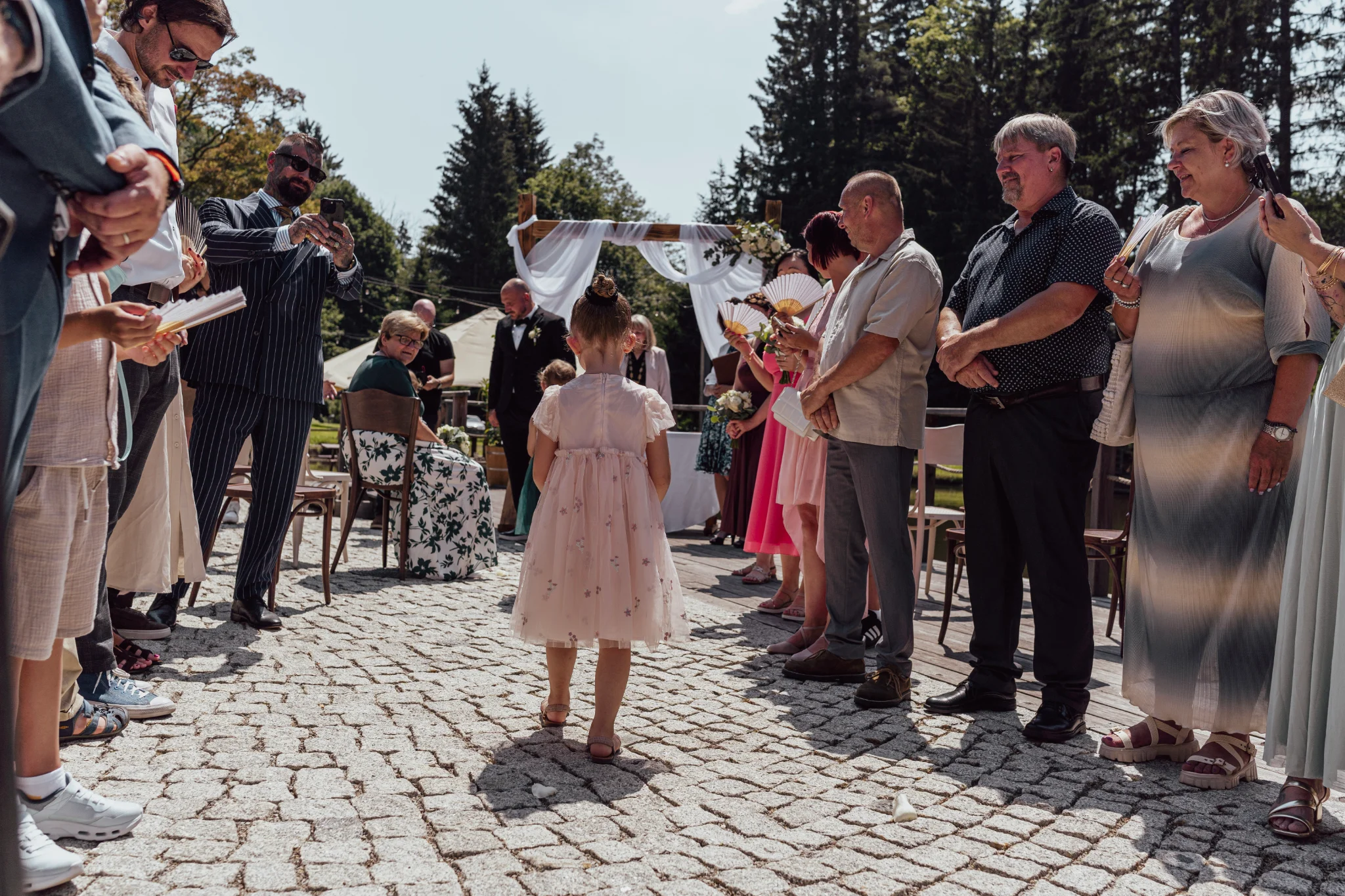 Little girl photographed from behind, walking down the aisle in front of the bride with flower petals.