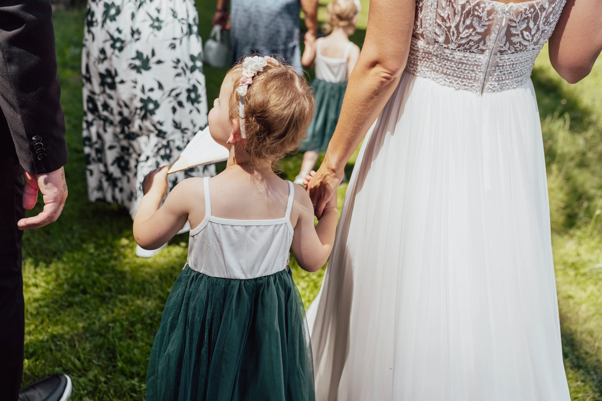 Bride holding her little daughter’s hand as they walk together, both photographed from behind.