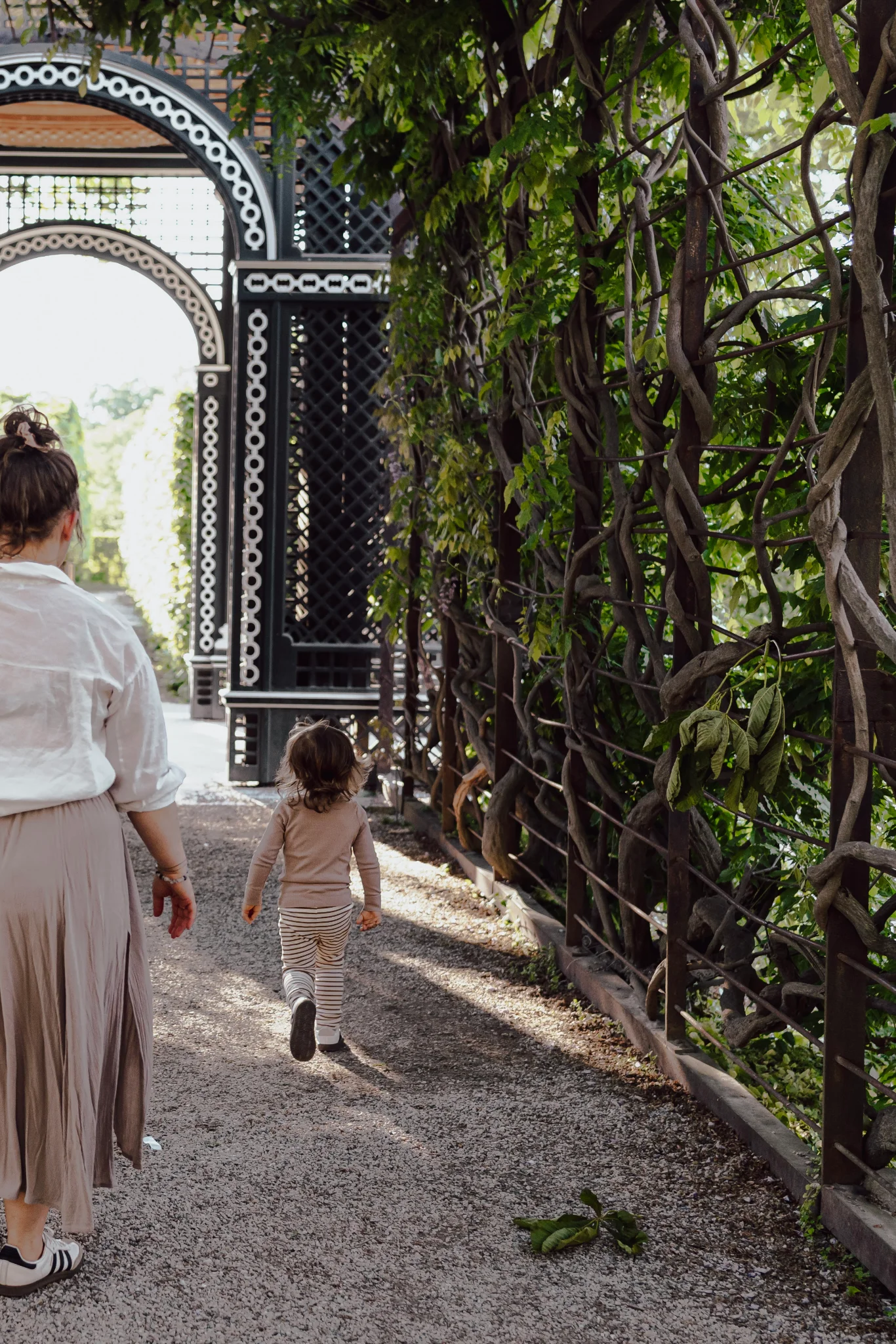 Mother and her little boy walking beneath a pergola in the gardens of Schönbrunn Palace, photographed from behind.