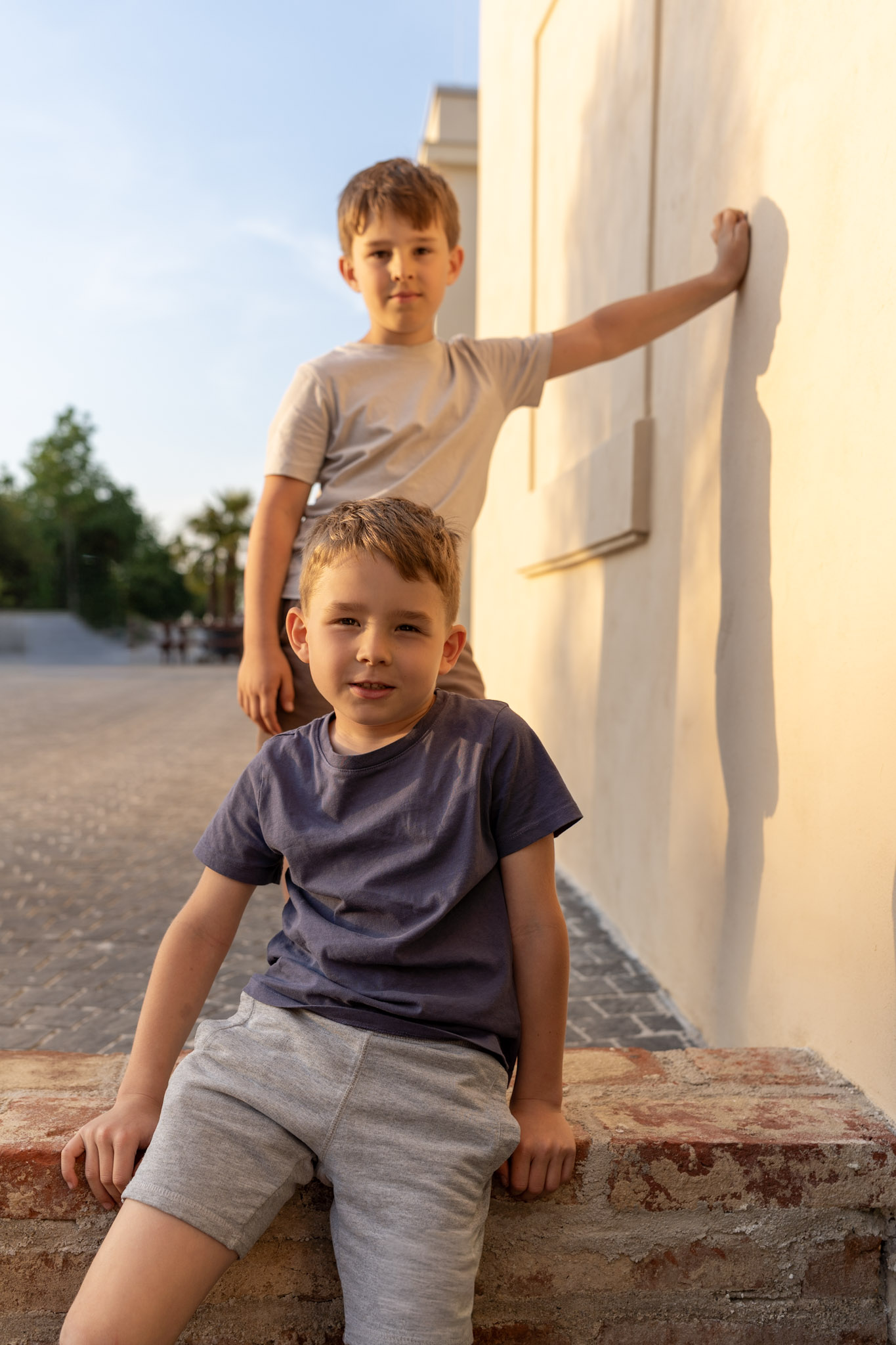 Brothers on a stone wall, the younger one sitting while the older one stands behind him.