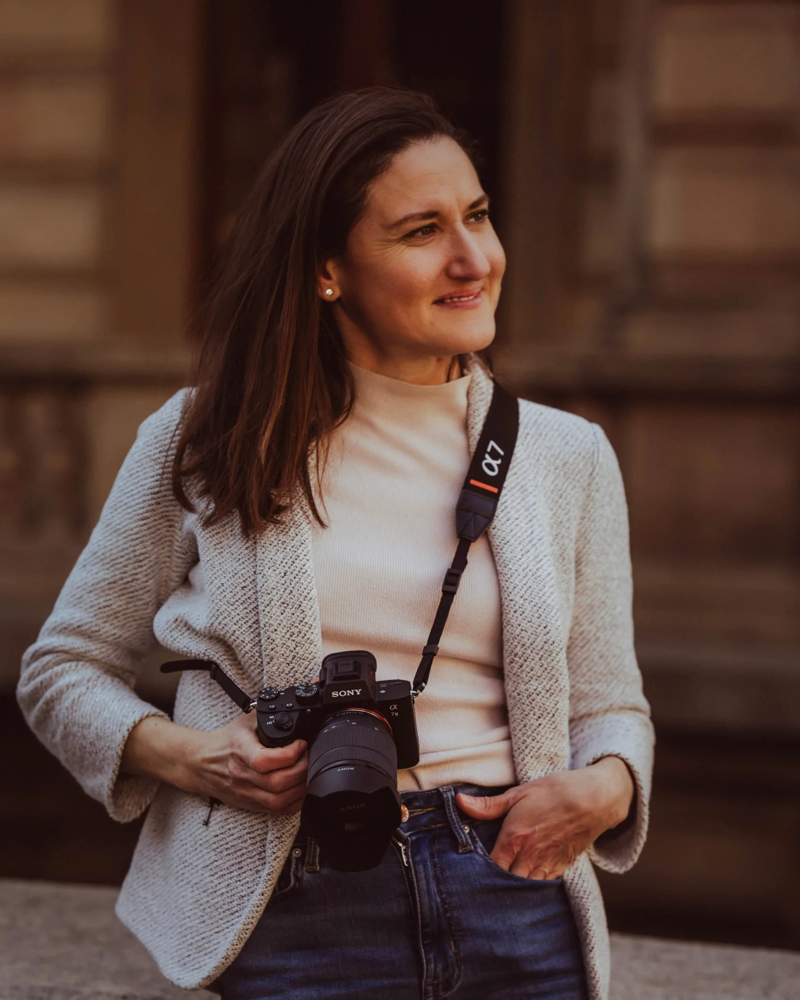 Photographer standing in the shade of a building with a camera in her hand.